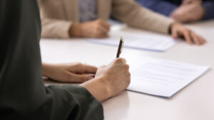 Close-up of a hand writing with a pen on documents at a desk